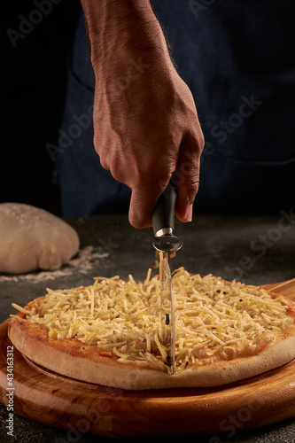 Vertical shot of a male's hand cutting delicious pizza with cheese and maize with a pizza knife