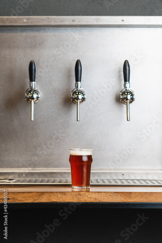 Beer with foam in glass jug against row of taps in bar on gray background