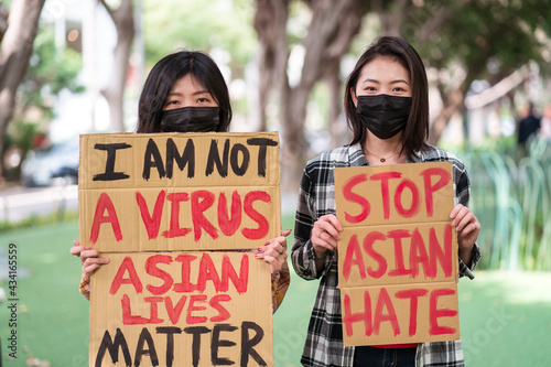 Ethnic females in masks holding posters protesting against racism in city street and looking at camera