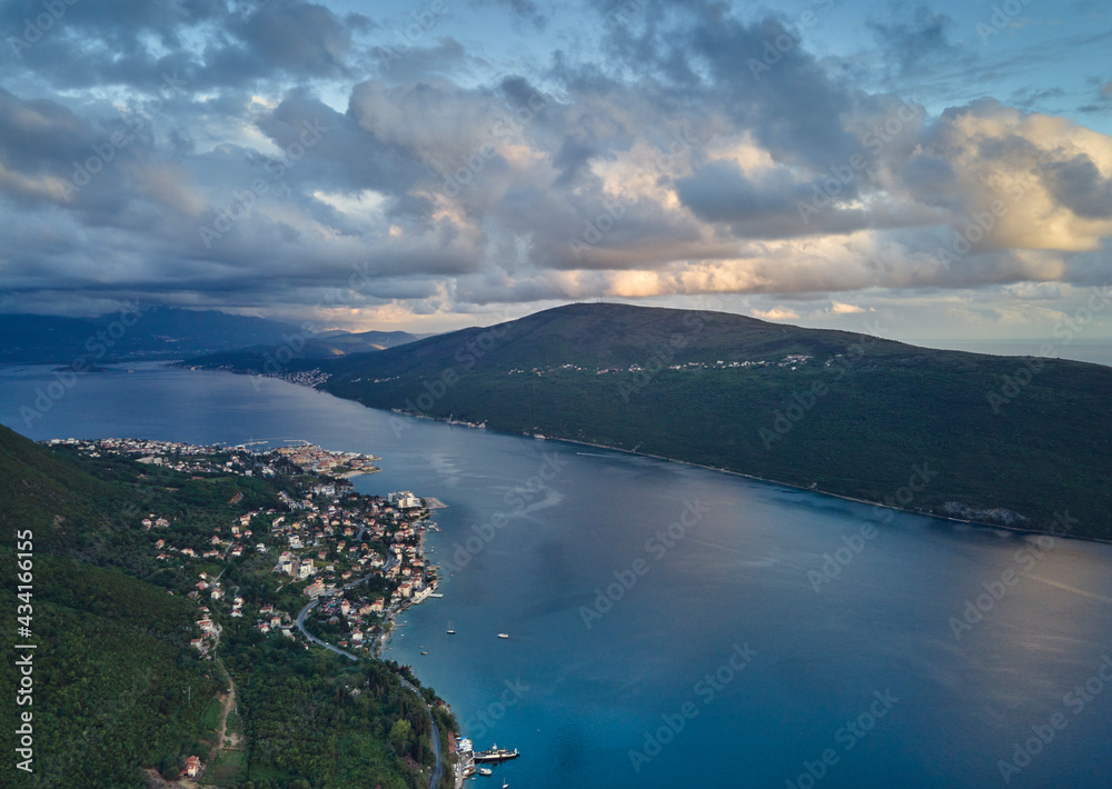 View of the Bay of Kotor, Zelenika and the peninsula of Lustica in Montenegro, with mountains and clouds at sunset.