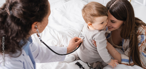 african american pediatrician in white coat examining baby boy with stethoscope, banner