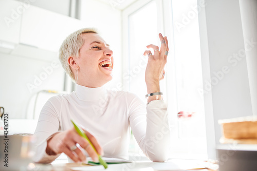 Happy female astrologist with short hair in rings looking away at desk on sunny day photo