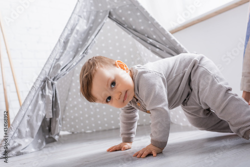 baby boy in romper crawling near tipi at home photo