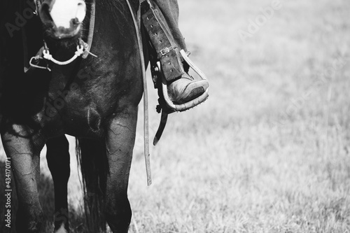 Western lifestyle concept with cowboy boot in stirrup while riding horseback in black and white, copy space on blurred field background. photo