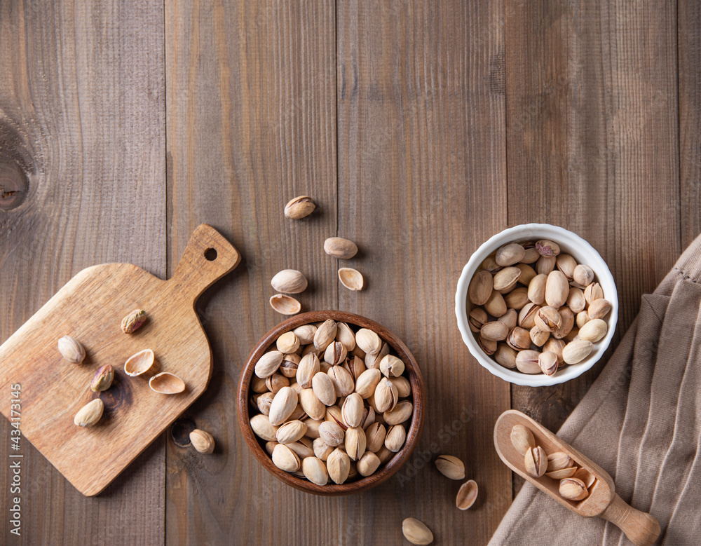 Flat lay pistachio nuts in bowls, on a cutting board and in a spoon on a brown wooden background. Top view and copy space Flat lay pistachio nuts in bowls, on a cutting board and in a spoon on a brown wooden background. Top view and copy space