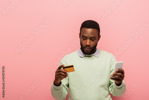 African american man using credit card and smartphone during online shopping on pink background