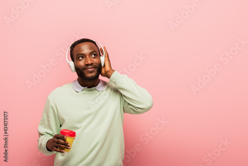 African american man in headphones holding paper cup on pink background