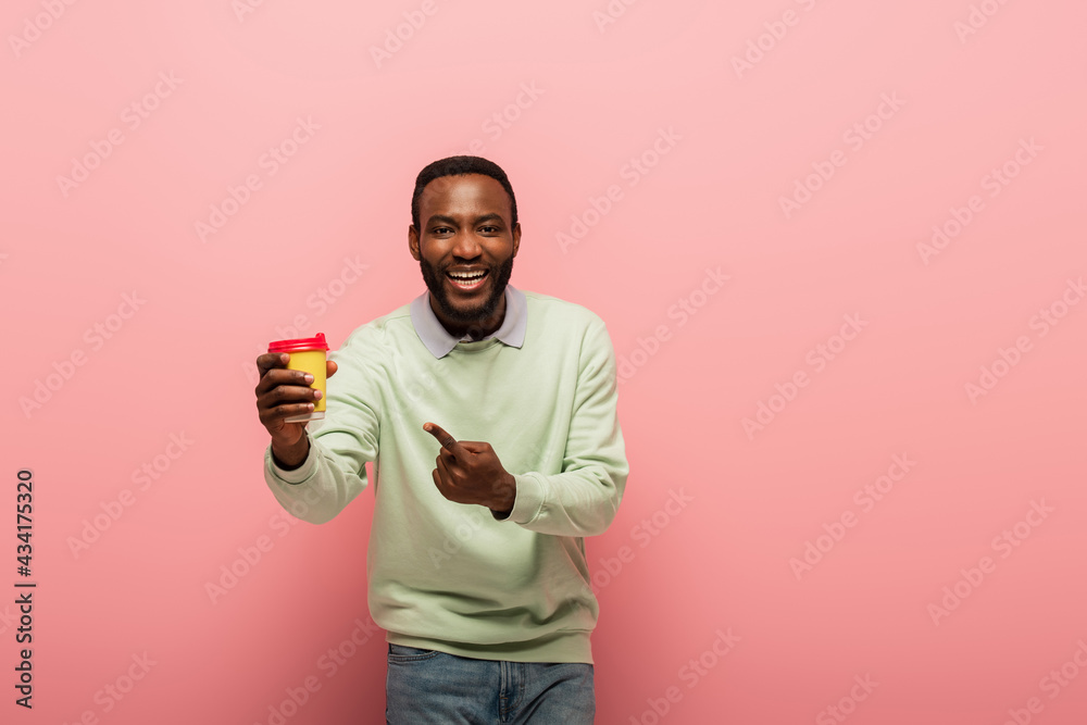 Smiling african american man pointing at paper cup on pink background Smiling african american man pointing at paper cup on pink background