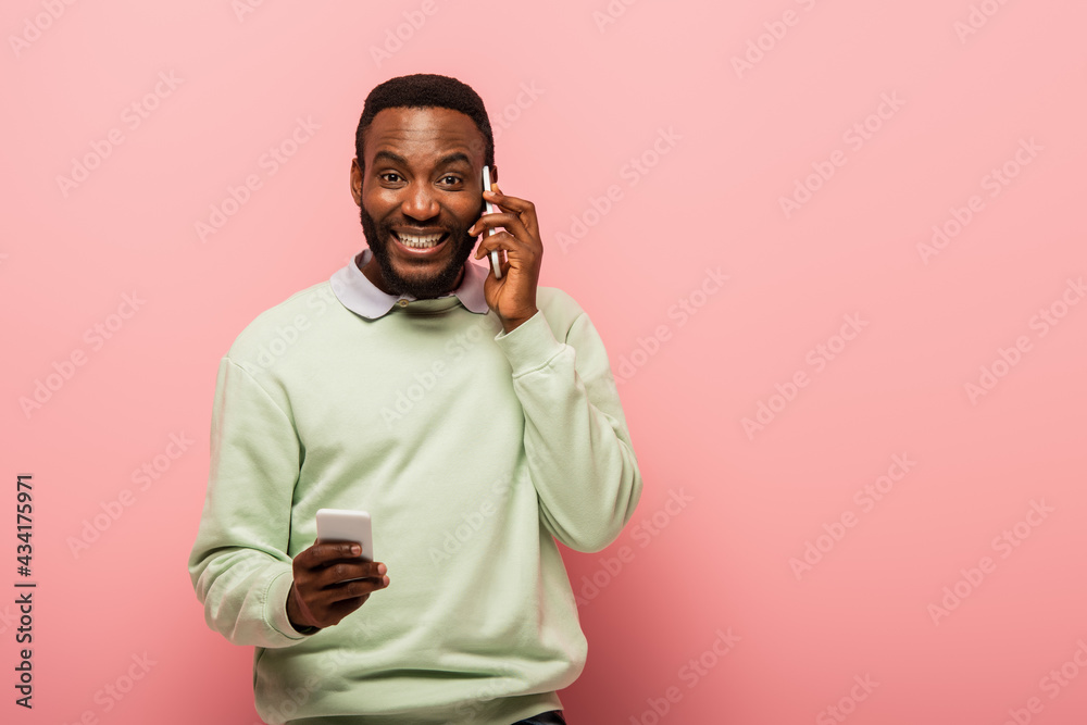 Smiling african american man holding smartphone during conversation on pink background Smiling african american man holding smartphone during conversation on pink background