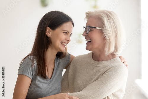 Smiling mature Caucasian mother have fun laugh and joke with excited adult teenage daughter. Happy overjoyed middle-aged mom enjoy family weekend leisure time with grownup teen child at home.