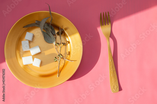 sugar cubes and dried roses on a golden plate, top view on a pink background. Space for the text. vegetarian diet