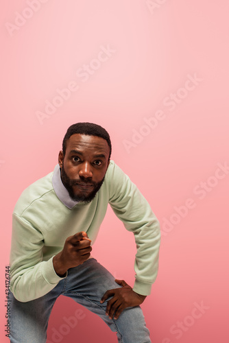 Young african american man pointing at camera isolated on pink