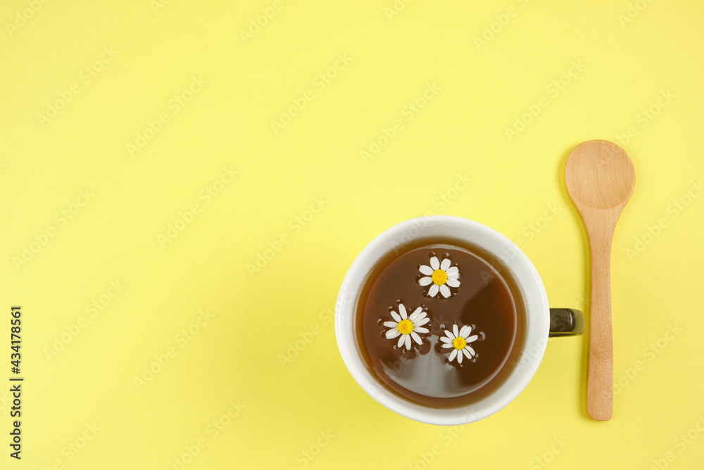 Cup with an infusion or chamomile tea on yellow background and a wooden spoon with space for text and full depth of field