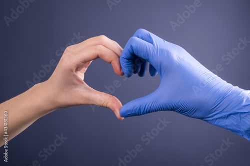 Hands of a doctor in medical gloves in the shape of a heart on a blue background. Patient and doctor's hand. Banner for website with copy space.