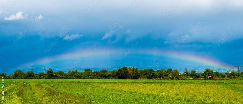 Naklejka premium Rainbow in dark blue sky over landscape
