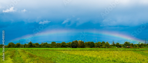 Rainbow in dark blue sky over landscape © Gabdulvachit