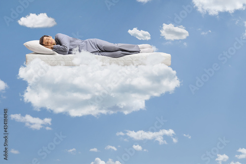 Man in pajamas sleeping on a mattress and floating on clouds photo