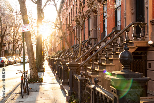 Block of historic brownstone buildings on Charles Street in the West Village neighborhood of New York City with afternoon sunlight shining on the empty sidewalk with no people photo