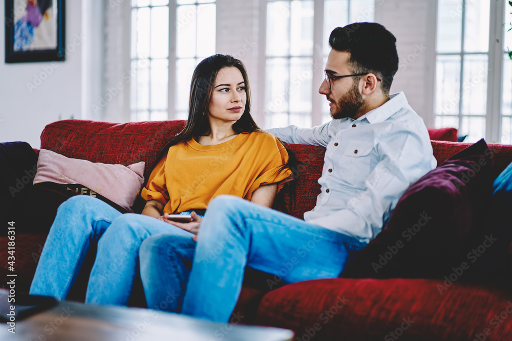 Multicultural couple in love talking and discussing plans during weeknd time in apartment, Turkish boyfriend communicating with Caucasian girlfriend resting at cozy sofa in stylish living room Multicultural couple in love talking and discussing plans during weeknd time in apartment, Turkish boyfriend communicating with Caucasian girlfriend resting at cozy sofa in stylish living room