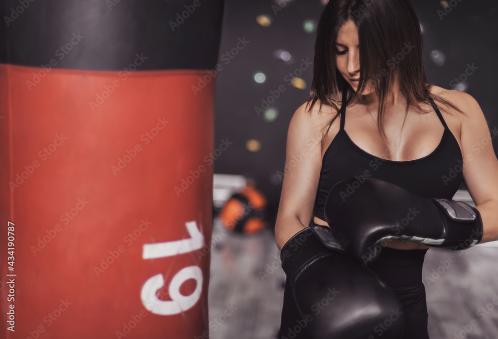 girl tightens her boxing gloves before a training session. she wears gloves and a black leotard. fitness and healthy living concept.