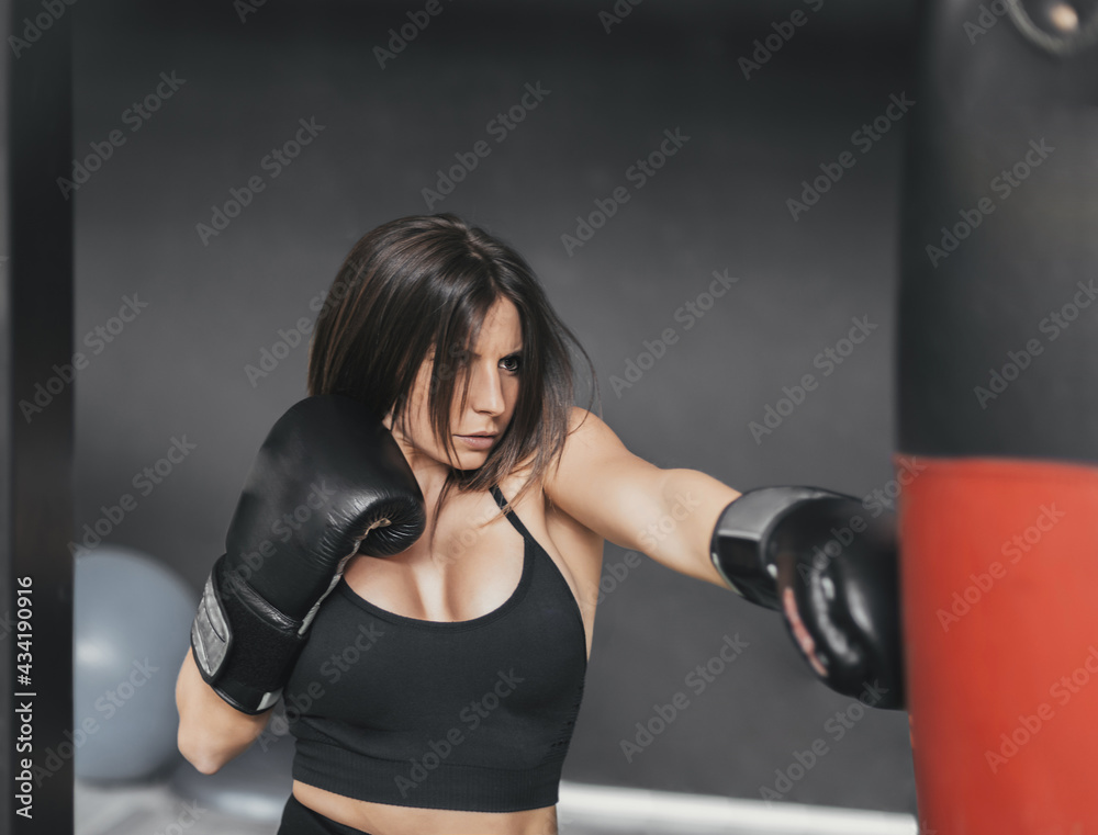 girl practicing boxing with a red bag. she is concentrating on her training. her boxing gloves are black.