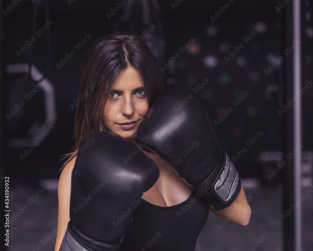 a boxer girl in defense position. she has black gloves. the background is dark gray. her light skin stands out against the background. she is smiling