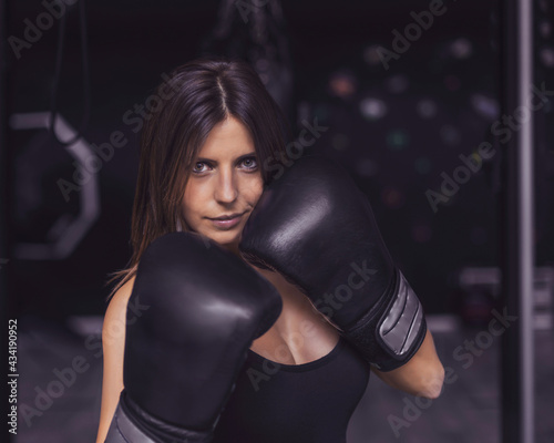 a boxer girl in defense position. she has black gloves. the background is dark gray. her light skin stands out against the background. she is smiling