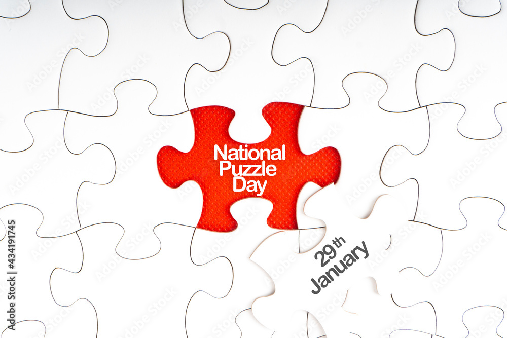 NATIONAL PUZZLE DAY text with jigsaw puzzle on red background. Education and Holiday Concept NATIONAL PUZZLE DAY text with jigsaw puzzle on red background. Education and Holiday Concept