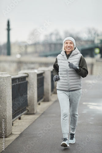 Εκτύπωση καμβά Cheerful beautiful senior woman in hat and gloves using smart watch while brisk