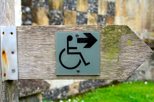 A disabled entry sign on a wooden arrow with old stone in the background of a village churchyard.