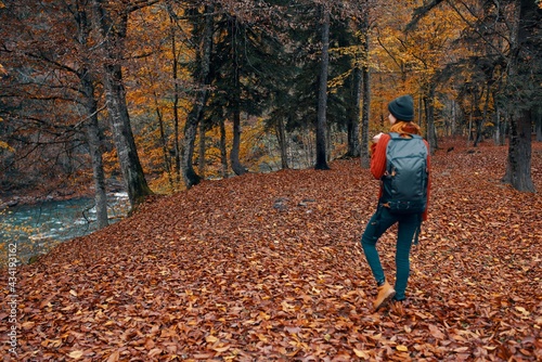 a full-length traveler with a backpack walks in the park with fallen leaves near the river