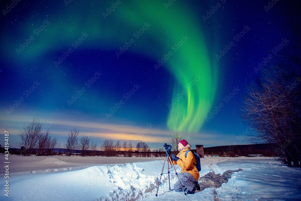 Concept photo tour to arctic travel, photographer man with camera and tripod photographs aurora borealis, northern lights green - obrazy, fototapety, plakaty 