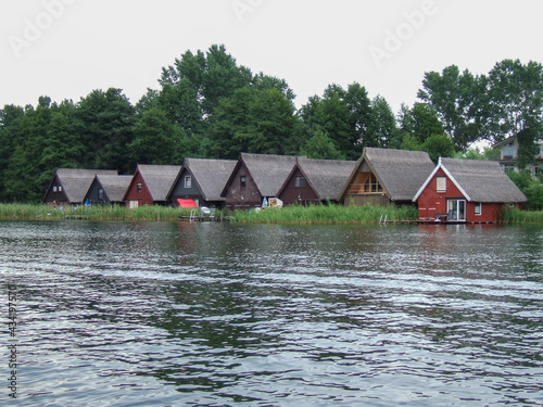 Some colorful fishermen houses on the inland lake Müritz in Mecklenburg Vorpommern. Reeds grow in front of the wooden houses and some jetties reach into the lake. Behind the thatched roofs are trees