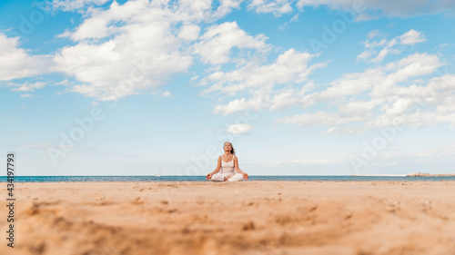 Senior woman in lotus pose sitting on the sand - Yoga at beach - Calm and meditation concept	