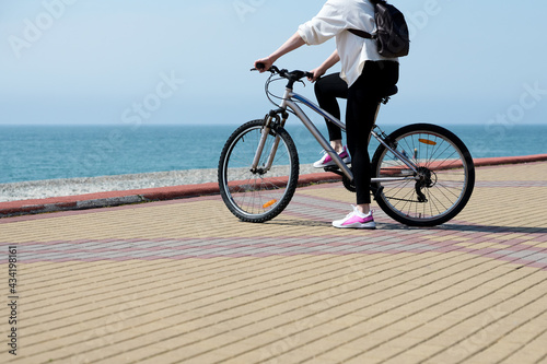  A girl in pink sports shoes on a morning bike ride along the sea embankment. Copy space.