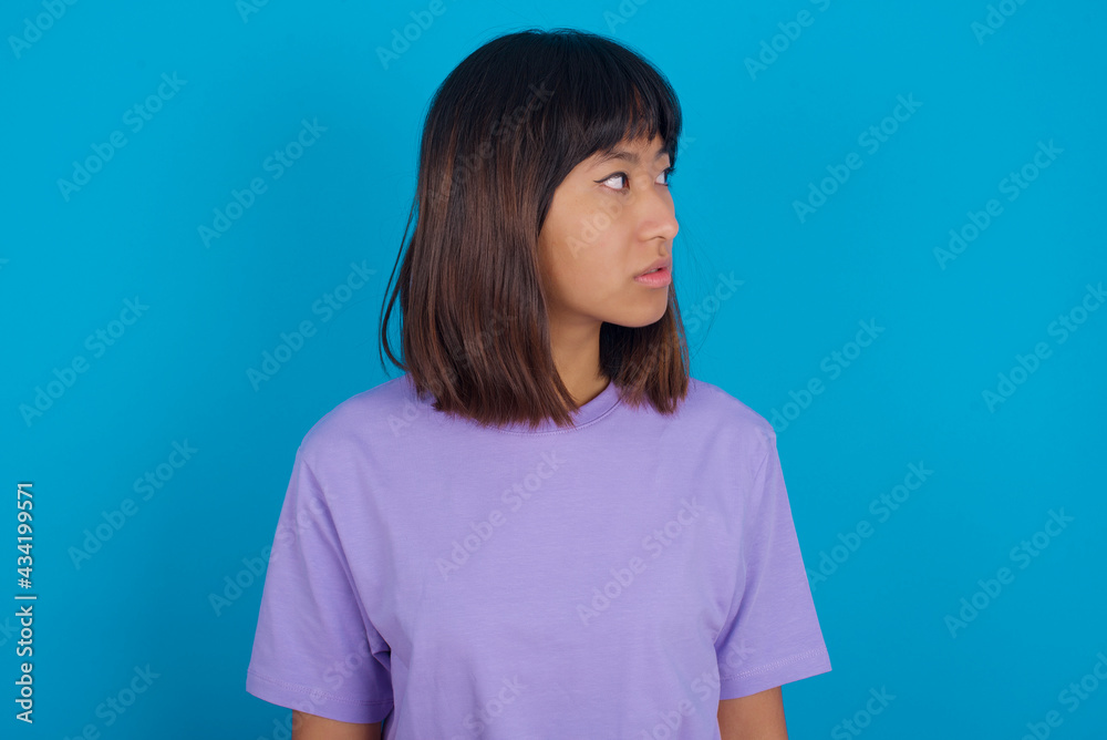 Close up side profile photo young beautiful asian woman wearing purple t-shirt against blue wall not smiling attentive listen concentrated
