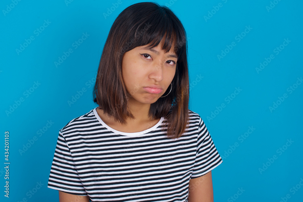 young beautiful asian woman wearing stripped t-shirt against blue wall depressed and worry for distress, crying angry and afraid. Sad expression. young beautiful asian woman wearing stripped t-shirt against blue wall depressed and worry for distress, crying angry and afraid. Sad expression.