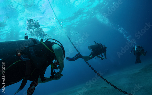 Wallpaper Mural Close up photo of three divers swimming after each other close to anchor chain in blue water. Light at surface, air bubbles from underwater breathing. Tropical Scuba Sea Divers Torontodigital.ca