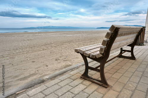 Great sea view, and beach together with wooden bench and its metal side exposed to corrosion and remainings of corrosion. Magnificent sky background. Street bench standing on cobblestone pathway.