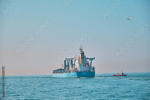 Huge transportation ship  (MAERSK) passing through in istanbul bosphorus during early in morning with small fishing ship and single seagull flying.