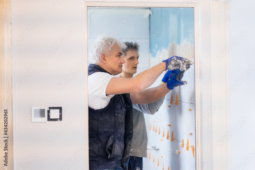Two tilers installing wall tile at home. Father and son laying tiles on