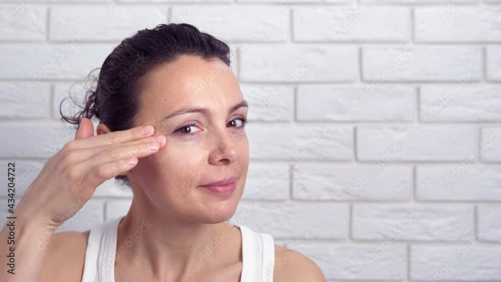 Dissatisfied woman with her skin. A woman with wrinkles touch her face on camera in the room. Dissatisfied woman with her skin. A woman with wrinkles touch her face on camera in the room.