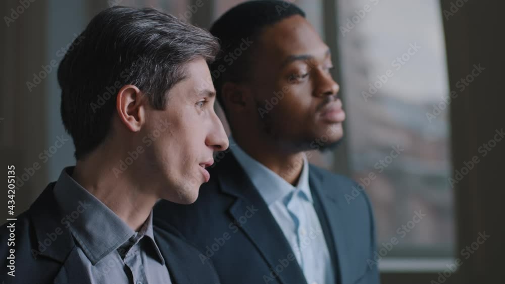 Portrait of two multiracial businessmen multinational colleagues looking out window pointing fingers discussing plan for future building, Caucasian investor and African architect talking about project Portrait of two multiracial businessmen multinational colleagues looking out window pointing fingers discussing plan for future building, Caucasian investor and African architect talking about project