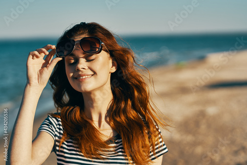 portrait of happy red-haired woman in nature on the beach near the sea and glasses on her face