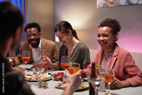 Diverse group of young people at dinner table laughing happily while enjoying party at home