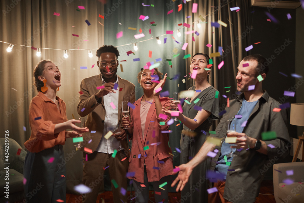 Diverse group of young people dancing under confetti shower while enjoying party with friends indoors