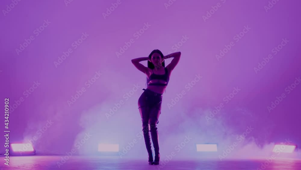 Silhouette of sexy brunette woman in black leather lingerie is sensually dancing in dark smoky studio with purple lights. Stripper moves erotically, waves hair, caresses attractive body. Slow motion. Silhouette of sexy brunette woman in black leather lingerie is sensually dancing in dark smoky studio with purple lights. Stripper moves erotically, waves hair, caresses attractive body. Slow motion.