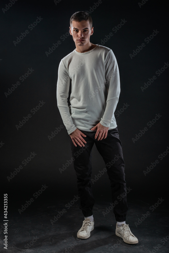 Fashion portrait on a black background of a handsome male model in white blouse and black pants