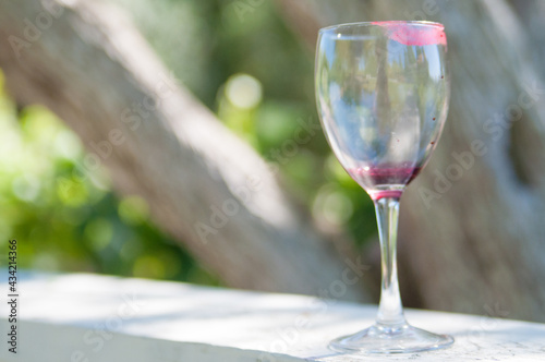 Lipstick marks an empty wine glass with traces of red wine, in a beautiful park setting
