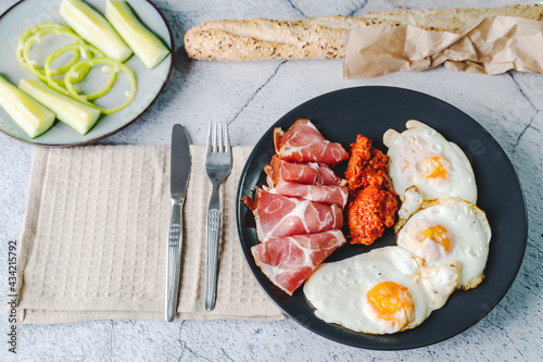 Top angle view on sunny side up eggs prosciutto coppa Capocollo dry meat and homemade ajvar paprika salad on the table as dinner or breakfast meal